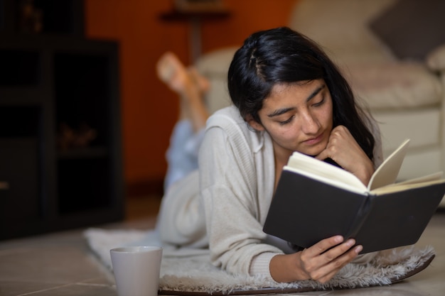 Vrouw latina liggen kijken naar de kant met boek met kopje koffie