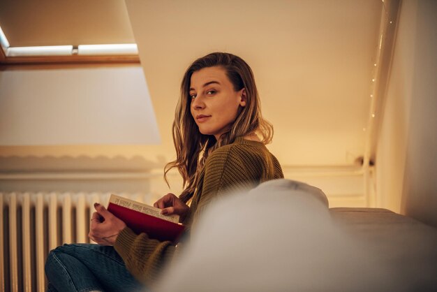 Vrouw leest een boek terwijl ze thuis op de bank zit