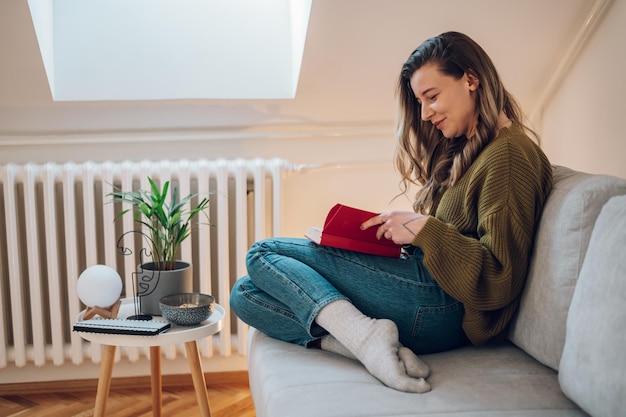 Vrouw leest een boek terwijl ze thuis op de bank zit