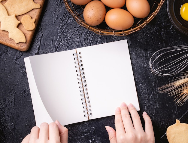 Vrouw leest kookboekrecept voor het maken van halloween-koekjes met bakingrediënten, ontwerpconcept van kookles, bovenaanzicht, plat leggen, overhead.