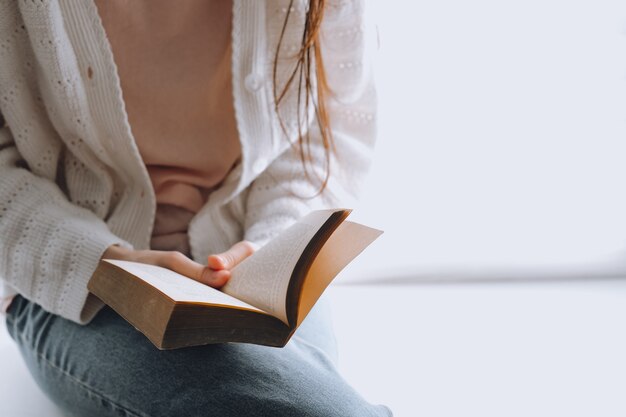 Vrouw leest overdag thuis een boek bij het raam.