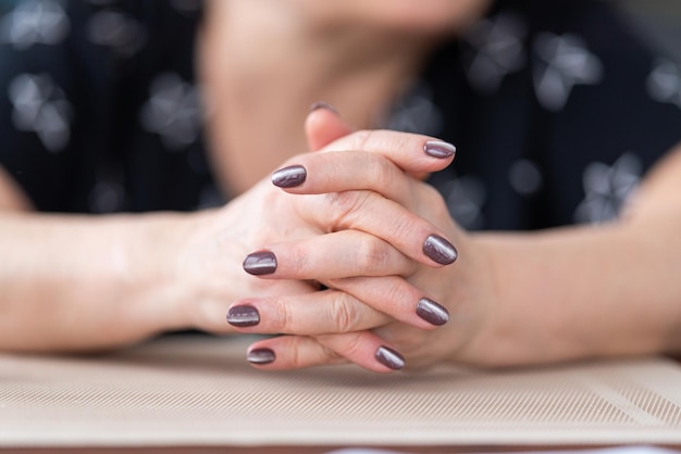 vrouw legde haar handen in elkaar, vingers verstrengeld. Vingers gevouwen, handen rustend op de tafel