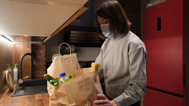 Foto vrouw legt productzakken op tafel en doet het masker thuis af