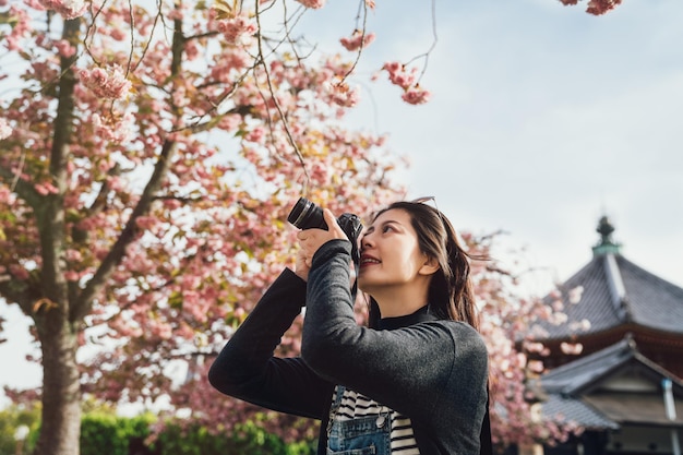 vrouw lens man met slr camera inzoomen nemen foto van prachtige bloeiende kersenboom met kofukuji op achtergrond. jonge aziatische fotograaf die in het voorjaar roze sakura in nara japan fotografeert.