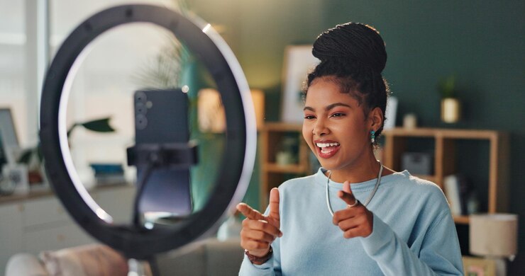 Foto vrouw licht en telefoon voor vloggen in de woonkamer glimlach en vingers voor ja aankondiging online vrouwelijke influencer en website thuis met mobiele creatieve beoordeling voor publiek met media tech