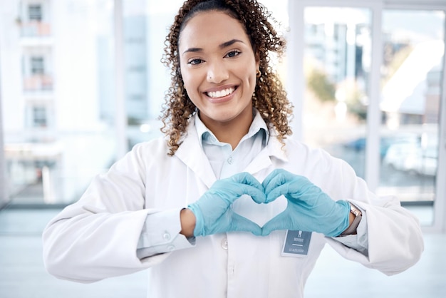 Vrouw liefde en hart handen portret in het ziekenhuis voor zorg vertrouwen en steun op valentijnskaarten Gezondheidszorg tandarts en gelukkige zwarte vrouwelijke arts met handgebaar voor genegenheid romantiek en vriendelijkheid