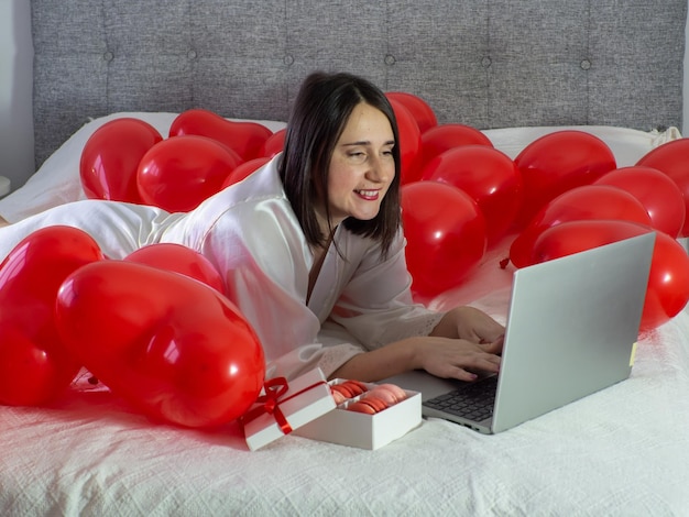 Vrouw liggend op bed met rode ballonnen voor Valentijnsdag feest
