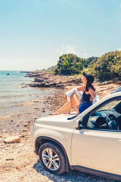 Vrouw liggend op de motorkap van de auto met uitzicht op zee zomer strand vakantie kopie ruimte