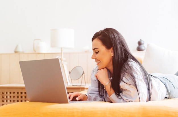 Vrouw liggend op een bank thuis te concentreren als ze op een laptop werkt