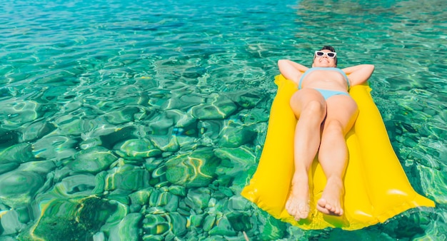Vrouw liggend op gele opblaasbare matras in blauw helder transparant zeewater