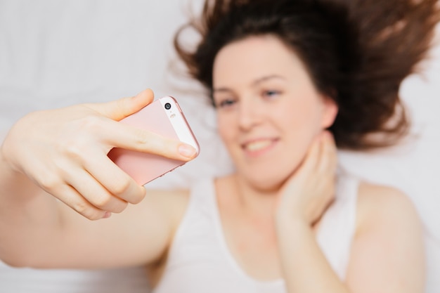 vrouw liggend op het bed maakt selfie aan de telefoon