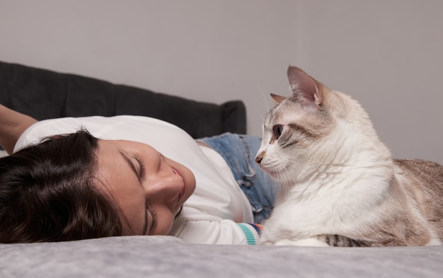 Foto vrouw liggend op het bed met haar wit gestreepte kat in een leuke pose naar elkaar kijken