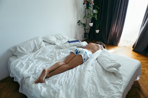 Vrouw liggend op het bed witte lakens licht uit raam met gordijnen