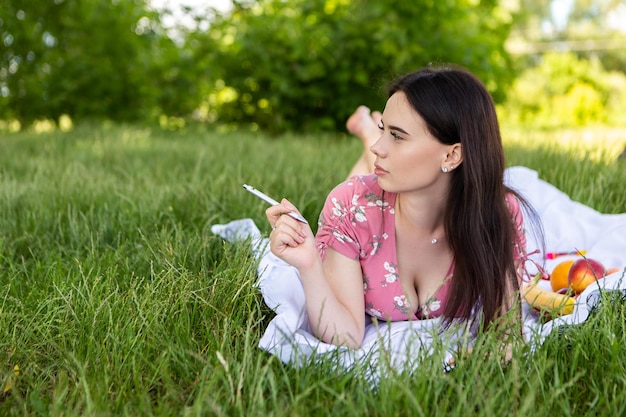 Vrouw liggend op wit bedsheet schrijven van notities met pen glimlachen Dame heeft een rust in het stadspark