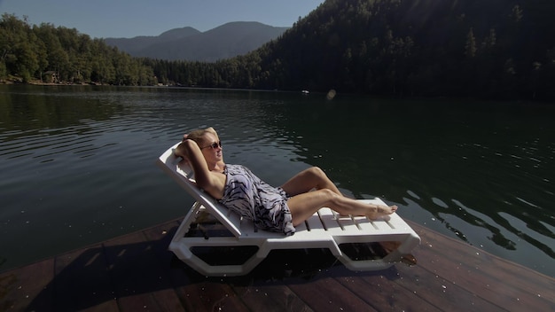 Vrouw ligt op een zonnebank in zonnebril en een boho zijden sjaal Meisje rust op een overstromingshouten onderwaterpier De stoep is bedekt met water in het meer