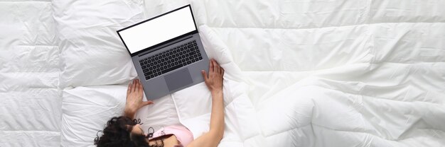 Vrouw ligt op wit bed met laptop.