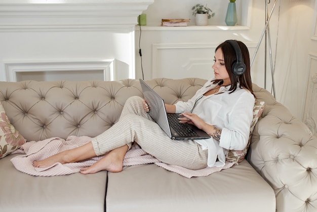 Vrouw ligt thuis op de bank met koptelefoon op en luistert naar muziek. Vrije dag thuis, relax en rust