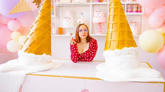 Vrouw lolly eten in zoetwaren Inhoud vrouw camera kijken terwijl het eten van zoete lolly op tafel met grote decoratieve ijshoorntjes in lichte zoetwaren