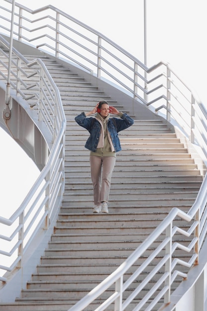Vrouw loopt de trap op en luistert naar muziek of podcast met rode koptelefoon in volle groei