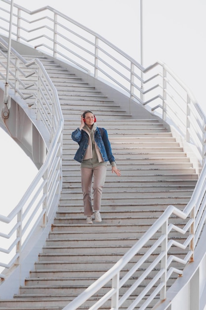 Vrouw loopt de trap op en luistert naar muziek of podcast met rode koptelefoon in volle groei