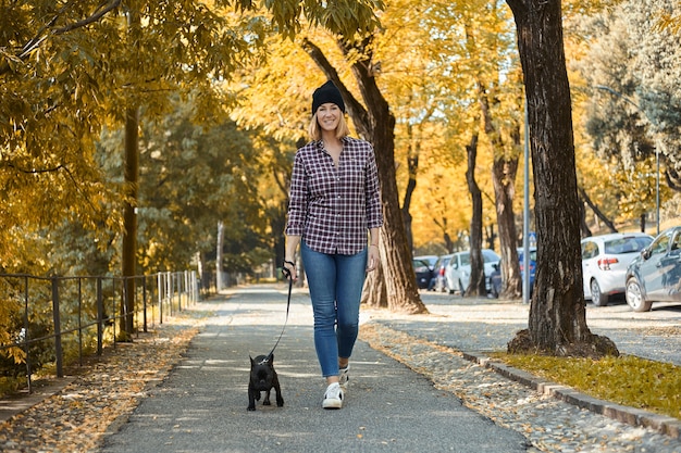 Vrouw loopt Franse Bulldog in herfstbladeren