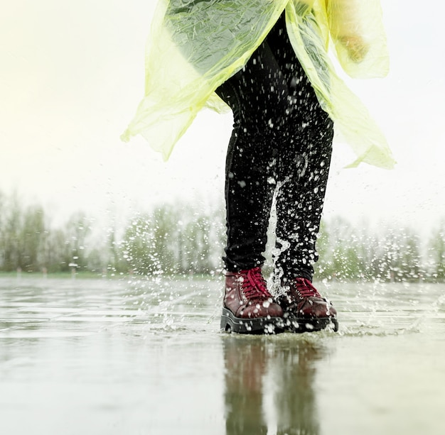 Foto vrouw loopt op asfalt bij regenachtig weer. close up van benen en schoenen spatten in plassen.