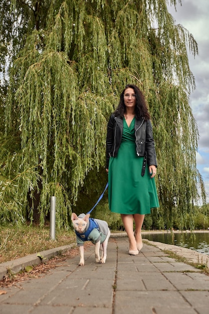 Vrouw lopen met kat aan de lijn buiten Concept van huisdierverzorging kat op harnas dagelijks wandelen joggen training en eventuele buitenrecreaties met mooi huisdier De eigenaar van het meisje draagt haar kat