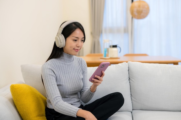 Vrouw luistert naar koptelefoon en leest thuis op mobiele telefoon