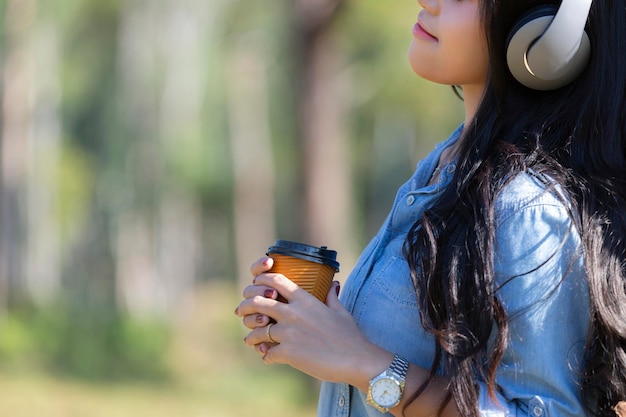 Foto vrouw luistert naar muziek terwijl ze koffie drinkt tegen bomen