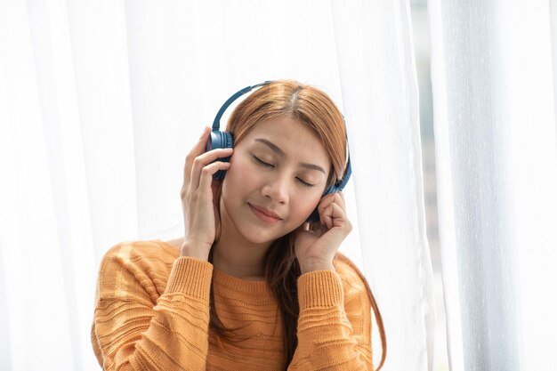 Vrouw luistert naar muziek terwijl ze thuis tegen het gordijn zit