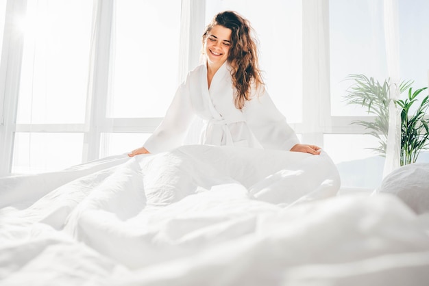 Vrouw maakt bed in de zonnige ochtend vrouw doet ochtend routine