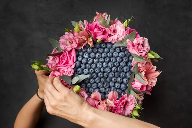 Vrouw maakt een boeket van bosbessen en roze bloemen in een cirkel