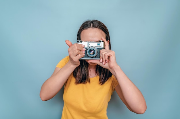 Vrouw maakt foto's met een oude filmcamera Gele laarskap zwart haar blauwe achtergrond