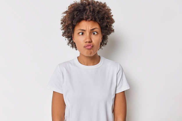 Vrouw maakt grimas kruist ogen en pruilt lippen probeert je te amuseren gekleed in casual t-shirt geïsoleerd op wit doet alsof ze dom is, toont zorgeloos gezicht. gezichtsuitdrukkingen