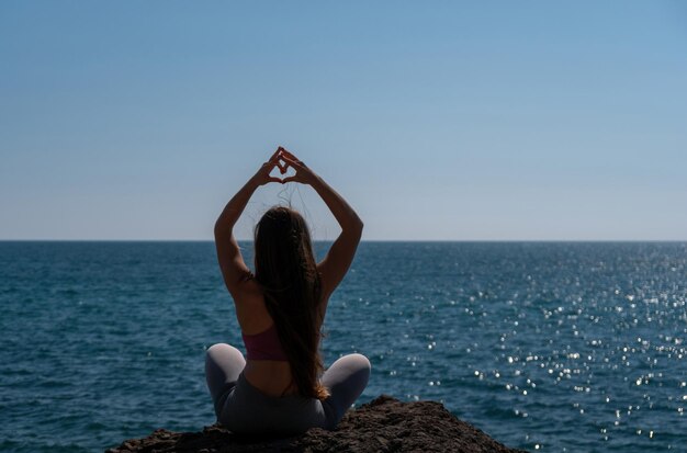 Vrouw maakt hart met handen op strand jonge vrouw met lang haar fitnessinstructeur die zich uitstrekt