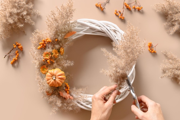 Vrouw maakt krans met oranje bloemen en droge natuurlijke materialen