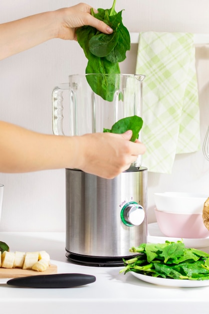 Foto vrouw maken groene spinazie detox smoothie met appel en kiwi met behulp van een blender. gezonde levensstijl