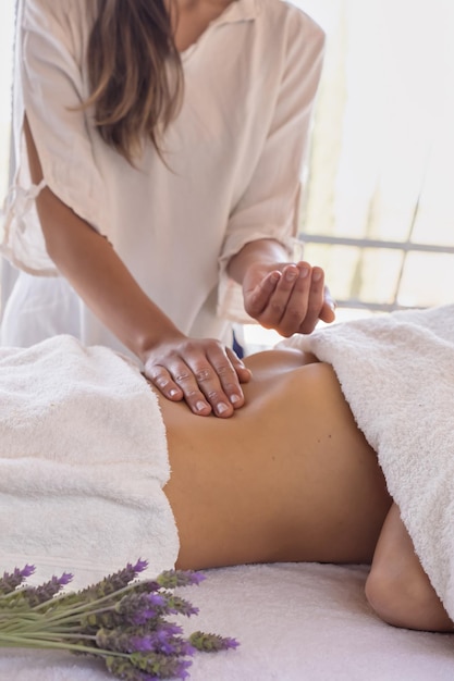 vrouw masseuse met patiënt op massagetafel olie op haar buik plaatsen close-up onherkenbaar