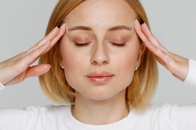 Vrouw mediteert en masseert haar slapen, sluit ogen, verlicht emotionele stress en nerveuze spanning, uitgeput door overwerk