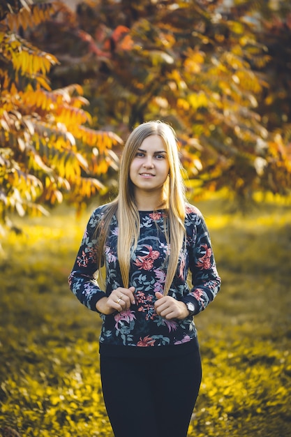 Vrouw meisje langharige blonde in een steegje met bomen met rode bladeren. Ze is gelukkig zelfverzekerd in een fotoshoot. Herfst park zonnige warme dag.