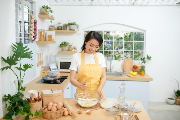 Vrouw mengt bloem met eieren tijdens het gebruik van een garde. Ze kookt bakkerij in huiselijke sfeer