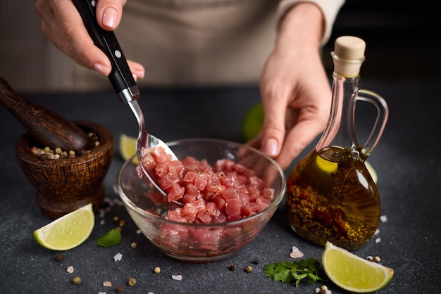 Vrouw mengt gesneden en gehakt tonijnfilet en specerijen in een glazen schaal en kookt traditionele tartare