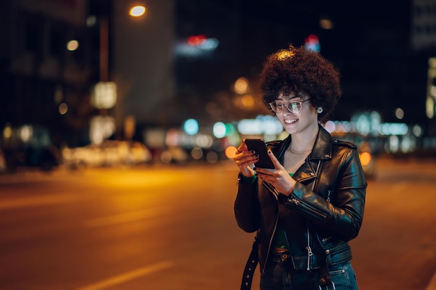 Vrouw met afrohaar die een smartphone buiten in de stad gebruikt