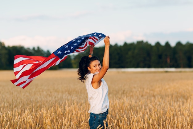 Vrouw met Amerikaanse vlag in tarweveld bij zonsondergang. 4 juli. Onafhankelijkheidsdag patriottische vakantie.