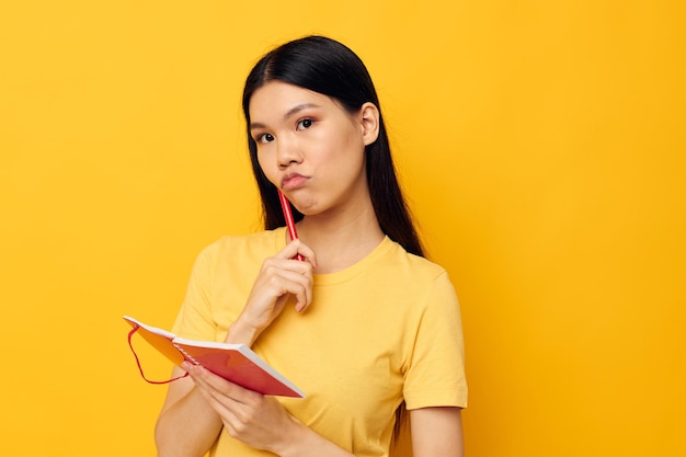 Vrouw met Aziatische verschijning in een geel t-shirt rood notitieboekje opleiding gele achtergrond ongewijzigd