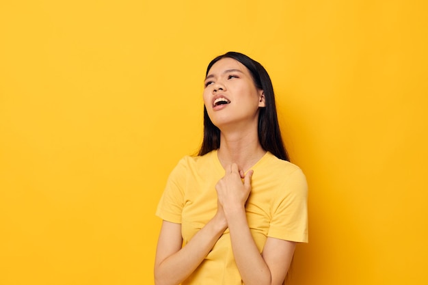 Vrouw met Aziatische verschijning in een gele t-shirt met zijn hoofd ontevredenheid gele achtergrond ongewijzigd