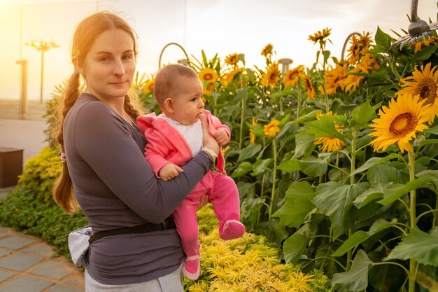 Vrouw met baby die van zonsopgang geniet in de tuin met zonnebloemen Baby op de handen houden