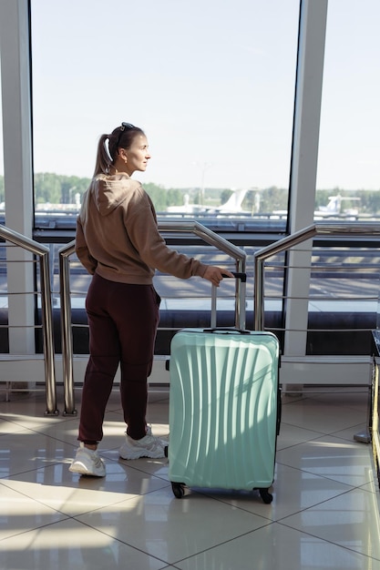 Vrouw met bagage die door het raam naar de luchthaventerminal kijkt