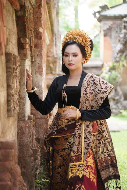 Vrouw met balinese kebaya die naast een reliëfmuur staat