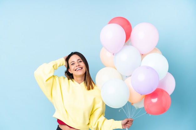 Vrouw met ballonnen in een partij over geïsoleerde blauwe muur lachen